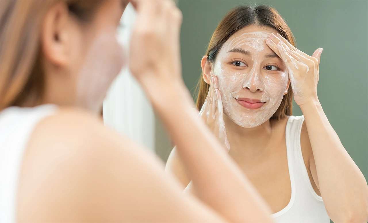 دختری که جلوی آینه ایستاده و صورت را با ژل شستشو می شوید
